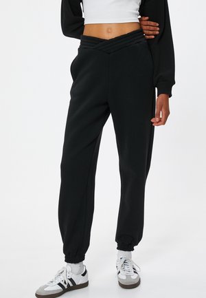 Zwarte joggingsbroek met een textuur, crossover tailleband, afgeknipte zoom en zijzakken, gecombineerd met witte sneakers. Vlotte stoffen textuur.