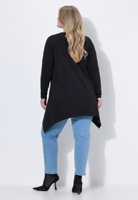 Czarna tunika z długim rękawem o asymetrycznym obrysie, zestawiona z jasnoniebieskimi jeansami ozdobionymi perełkami po bokach oraz czarnymi butami na wysokim obcasie.