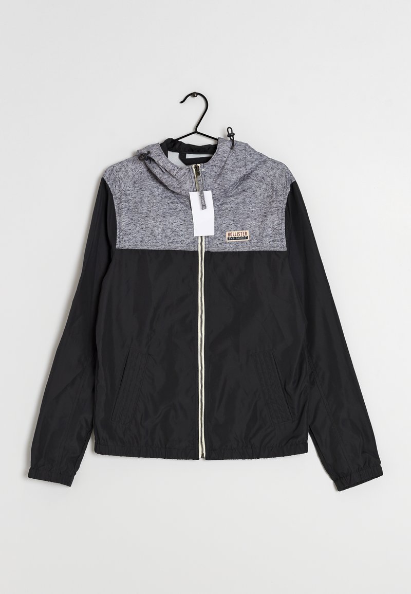 Black and gray hooded jacket with a zip front, featuring a textured gray upper, smooth black lower, and two side pockets.