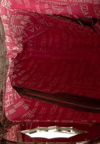 Vnitřek kabelky v jasně růžové tkanině, zdobený vzorem s logem. Obsahuje zipovou kapsu na jedné straně pro další úložný prostor.