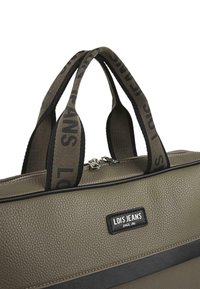 Bolso de hombro verde oliva, material texturizado, acentos negros, asas dobles en la parte superior con cinta de logo, cierre de cremallera, forma rectangular.