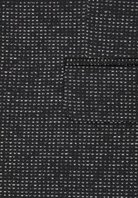 Tessuto testurizzato in nero con motivo maculato bianco. Presenta una tasca a toppa. Il materiale appare intrecciato con un design a griglia uniforme.
