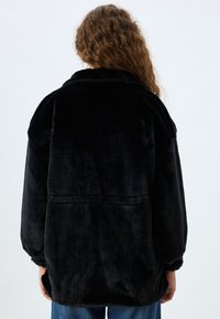 Sort faux fur jakke med afslappet pasform, oversized krave, elastiske manchetter og synlige sømdetaljer på ryggen. Blød tekstur og mat finish.