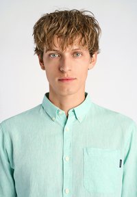 Miętowa koszula zapinana na guziki, wykonana z lekkiego materiału, z kieszonką na piersi i małą metką z logo po boku. Gładka tekstura, z kołnierzykiem.