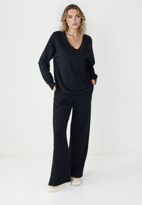 Haut noir à manches longues avec un col en V et une coupe décontractée, associé à un pantalon noir à jambes larges. Les deux vêtements sont en tissu doux et extensible.