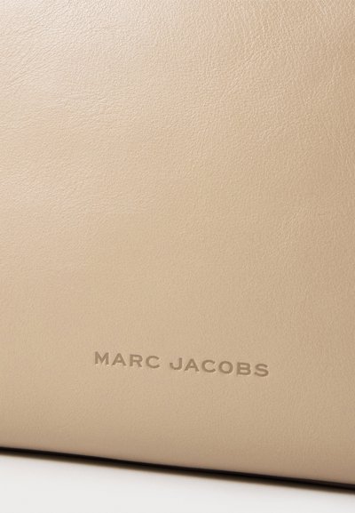 Surface en cuir beige avec une texture subtile et le nom de la marque Marc Jacobs embossé dans un ton assorti près du bas.