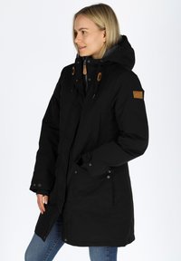 Black parka coat with a hood, featuring a zip and snap button closure, leather accents, and two side pockets. Smooth texture and warm design.