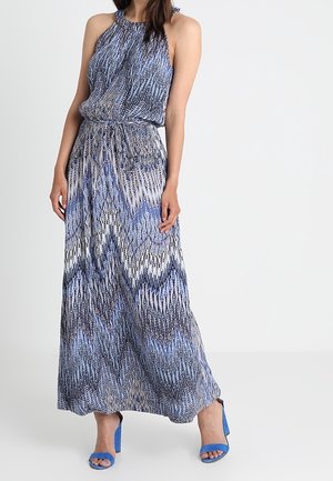 Maxikleid mit Neckholder, das ein blau-weißes Zickzackmuster aufweist. Leichter Stoff mit einem elastischen Taillenbund. Blaue High Heels.