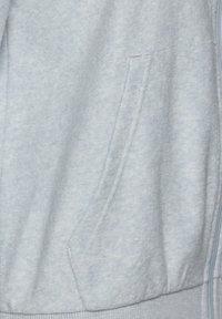 Helleblaue Kapuzenjacke aus weichem Material, mit einer Vorderentasche und geripptem Saum. Die Textur ist glatt mit leichten Farbvariationen.