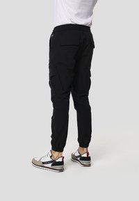 Pantalones cargo negros con puños elásticos, con bolsillos laterales y un ajuste relajado, combinados con zapatillas deportivas multicolores.