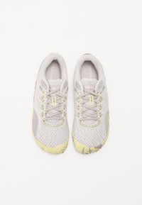 Baskets de sport gris clair avec tige en mesh, accents jaunes et semelle en caoutchouc texturé, présentant un design à lacets et un col rembourré.