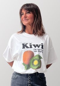 T-shirt bianco oversize con una grafica di due kiwi e il testo "VCL FRUIT & Co. Kiwi, sto aspettando la tua prole." Design frontale.