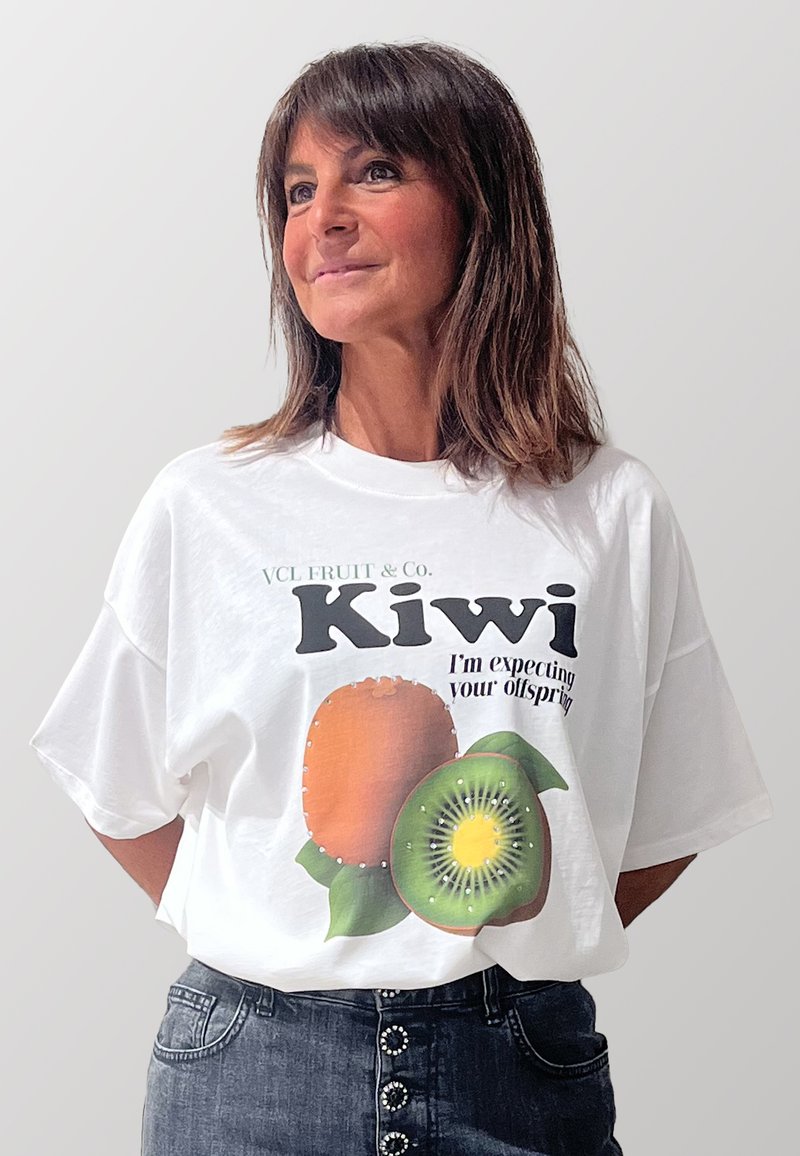 T-shirt bianco oversize con una grafica di due kiwi e il testo "VCL FRUIT & Co. Kiwi, sto aspettando la tua prole." Design frontale.