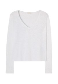 Bela majica z dolgimi rokavi in V-izrezom, rahlo teksturirane tkanine in z neobdelanim robom izreza, prikazana na enobarvnem ozadju.