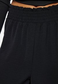 Zwarte broeken met een gestructureerde afwerking, voorzien van een elastische tailleband met geplooide details. Glad materiaal en losse pasvorm voor comfort.