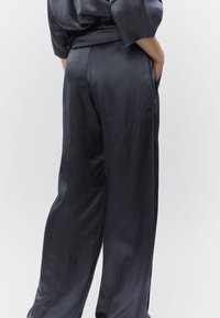 Σκούρο σατέν παντελόνι με φαρδιά μπατζάκια και λεία υφή, με πλαϊνές τσέπες και ρέουσα σιλουέτα. Λεπτή μέση με ζώνη και διακριτική λάμψη.