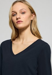 Maglietta a maniche lunghe blu navy con scollatura a V, realizzata in un tessuto morbido, caratterizzata da una vestibilità rilassata e da dettagli minimalisti.