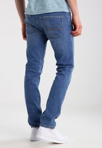 Blå denimjeans med slim fit, med bakfickor, ljus blekning och sömnadsdetaljer. Matchas med vita sneakers.
