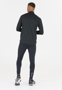 Svart långärmad träningsskjorta med hög krage, tillsammans med svarta leggings. Skorna har en mönstrad grå och svart design.