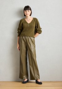 Pulover ribbed de culoare verde olive cu decolteu în V, asortat cu pantaloni amplați din piele ecologică verde olive, cu talie înaltă. Pantofi negri. Bijuterii simple din argint.