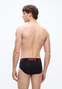 Fekete Nike férfi alsónadrág, széles rózsaszín logós derékpánttal, sima textúrával és testhezálló szabással, hátulnézetből.