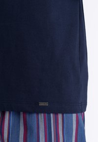 Mörkblå bomullströja med ett märke med "Hanro" på fållen, tillsammans med randigt blått och rött tyg nedanför, vilket visar kontraster i textur.