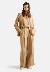 Béžový lněný oblek s dobře padnoucím sakem a volnými kalhotami. Sako má klopový límec a zapínání na knoflíky, doplněné o odpovídající košili.