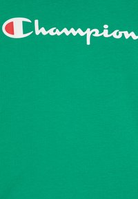 Roheline puuvillane T-särk, millel on suur valge "Champion" logo kõveras skripti stiilis rinnaosas. Sile tekstuur, klassikaline lõige.
