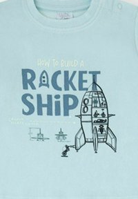Camisa de algodón azul claro con un gráfico de un cohete de dibujos animados y elementos de construcción, con el texto "Cómo construir un COHETE."