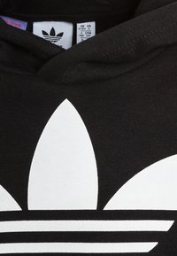 Felpa nera con cappuccio, caratterizzata da un grande logo trefoil bianco e strisce orizzontali. Il tessuto appare morbido, con una texture liscia e una vestibilità rilassata.