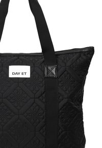 Kvadret svart tote-väska med tygstruktur, utrustad med starka svarta handtag och en vit etikett med "DAY ET"-logotypen högst upp.