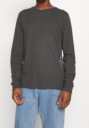 Camiseta de manga larga gris de algodón con escote redondo, detalle de logo lateral y corte holgado. Combinada con vaqueros azul claro.