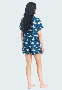 Conjunto de pijama de manga corta en azul con un patrón de nubes y estrellas. El material parece suave; la parte superior y los pantalones cortos tienen un ajuste relajado con acentos amarillos.