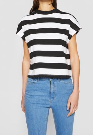 Woman wearing a black and white horizontal striped short-sleeve top with high-waisted blue jeans against a plain light background.