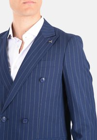 Giacca da abito doppiopetto navy con righe bianche, colletto a rever, due bottoni e spilla a forma di forbice argentata. Dettagli in tessuto testurizzato.