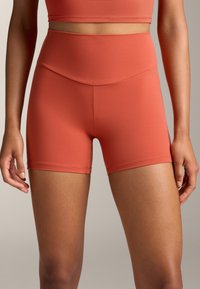 Magasan derekú, korall-narancssárga rövidnadrág rugalmas anyagból, sima felülettel, széles derékrésszel és minimális varrással.
