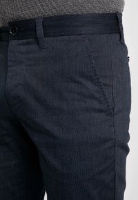 Navy blue trousers with a fine textured pattern, featuring a standard waistband, button closure, and front pockets.