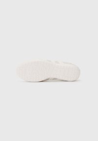 White sneaker sole featuring a textured pattern with ridges and embossed branding. The design is minimalistic and flat, suitable for casual wear.
