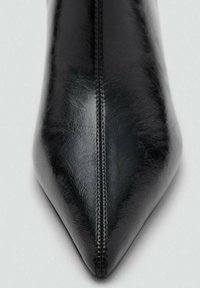 Bottine noire en cuir avec un bout pointu et une finition lisse, dotée d'un détail de couture centrale, présentant un design épuré et des accents matériels minimes.