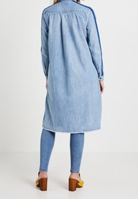 Ljusblå denimskjortklänning med långa ärmar, med sidostripes, fransad nederkant och avslappnad passform. Kombinerad med blå denimleggings.