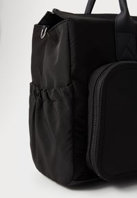 Zwarte nylon tas met een gestructureerd ontwerp, textuur oppervlak, voorzak met rits en zijzak met plooien voor accessoires.