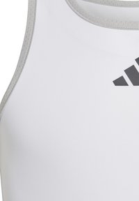 Biely športový tielko s šedými akcentmi, s okrúhlym výstrihom a jemnou textúrou. Na prednej strane sa nachádza čierne logo Adidas.