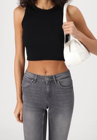 Top corto negro acanalado, jeans de mezclilla gris con bolsillos, textura suave. Bolsa blanca con diseño curvado y cierre de cremallera.