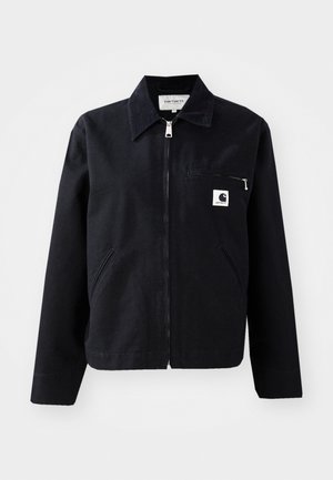 Zwarte canvasjas met een rits aan de voorkant, kraag, twee zijzakken en een borstzak. Heeft een klein wit vierkant logo op de zak.