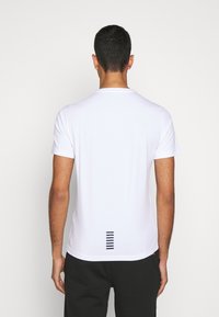 Camiseta blanca de manga corta con cuello redondo, que presenta un acento de rayas verticales en color marino en la parte baja de la espalda. Tejido de textura lisa.
