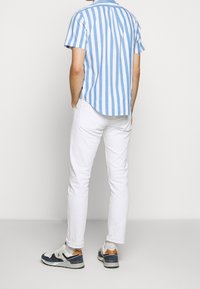 Modrobíle pruhované tričko s krátkým rukávem, bílé slim fit kalhoty a vícebarevné tenisky. Čistý design s ležérním vzhledem.