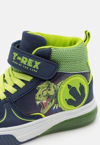 Adidași înalți, cu un exterior sintetic de culoare bleumarin, cu accente de plasă verde, șireturi de un verde strălucitor și un design imprimat cu T-Rex.