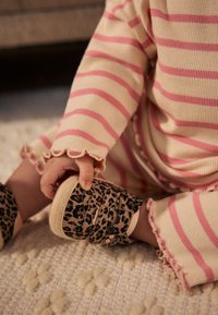 Juodi bateliai su leopardo raštais, smėlio atspalvio detalėmis ir elastinėmis juostelėmis. Vaikas dėvi rožinės spalvos dryžuotą, riestainiu kraštu ribos apdailą turintį rūbą.