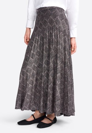 Woman wearing a high-waist, black and white patterned maxi skirt with black Mary Jane flats and a white long-sleeve shirt.