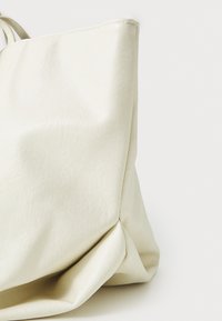 Sac fourre-tout de couleur crème en simili cuir texturé. Présente de douces plis et une couture minimale, avec une base structurée.